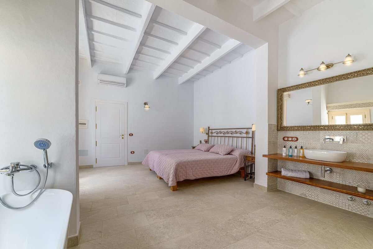 Ein Schlafzimmer mit Bett, ein Badezimmer mit Waschbecken und Spiegel sowie ein Oberlicht.