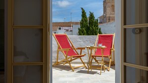 Puerta abierta que da a una terraza con dos sillones rojos y una mesita, con vistas a un edificio histórico con una cúpula roja.