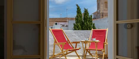 Puerta abierta que da a una terraza con dos sillones rojos y una mesita, con vistas a un edificio histórico con una cúpula roja.