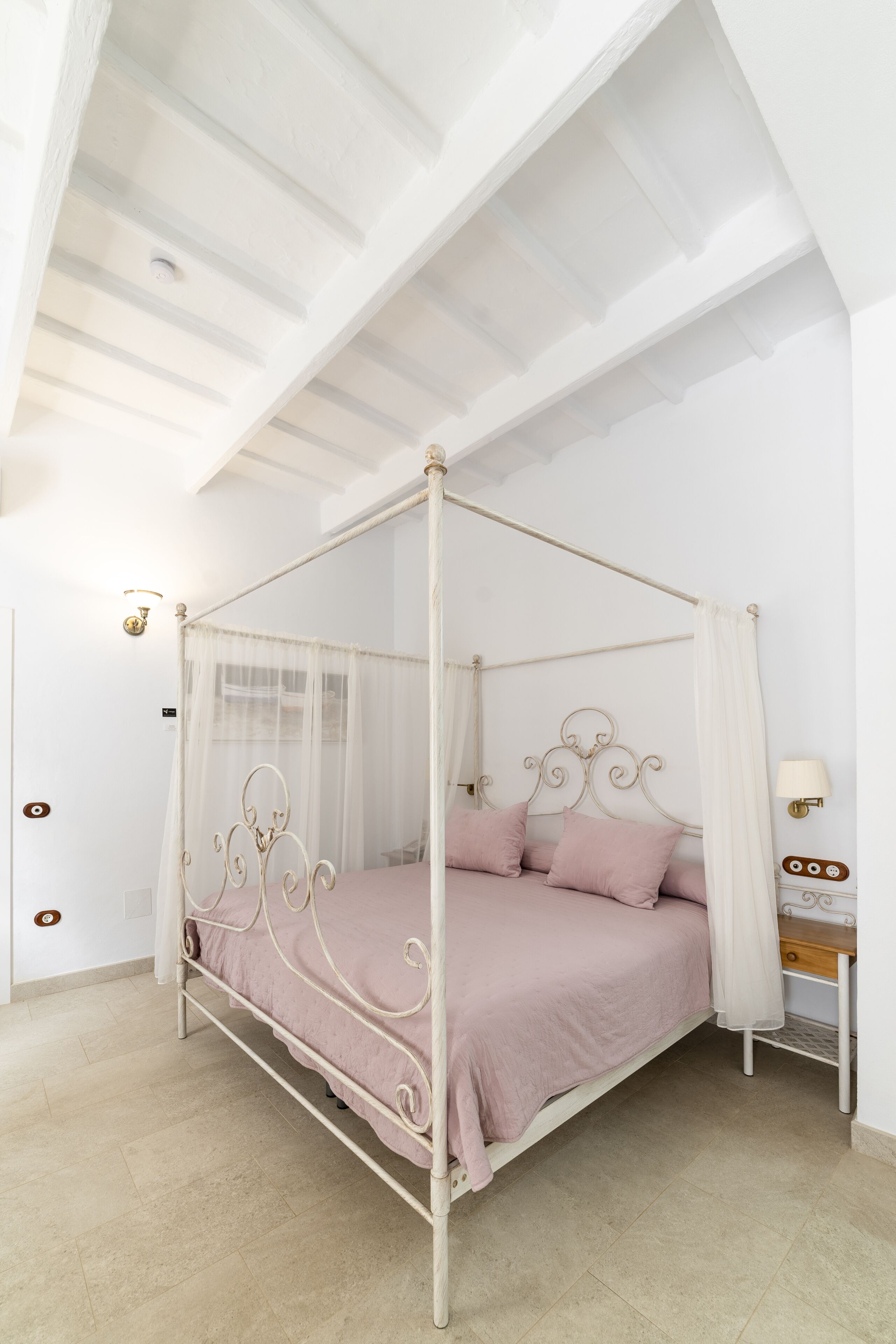 Una cama con dosel, una mesita de noche con lámpara y una lámpara de pared.
