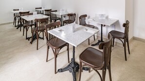 Un comedor con techo de piedra, paredes blancas y sillas de madera. Las mesas están dispuestas para sentarse.