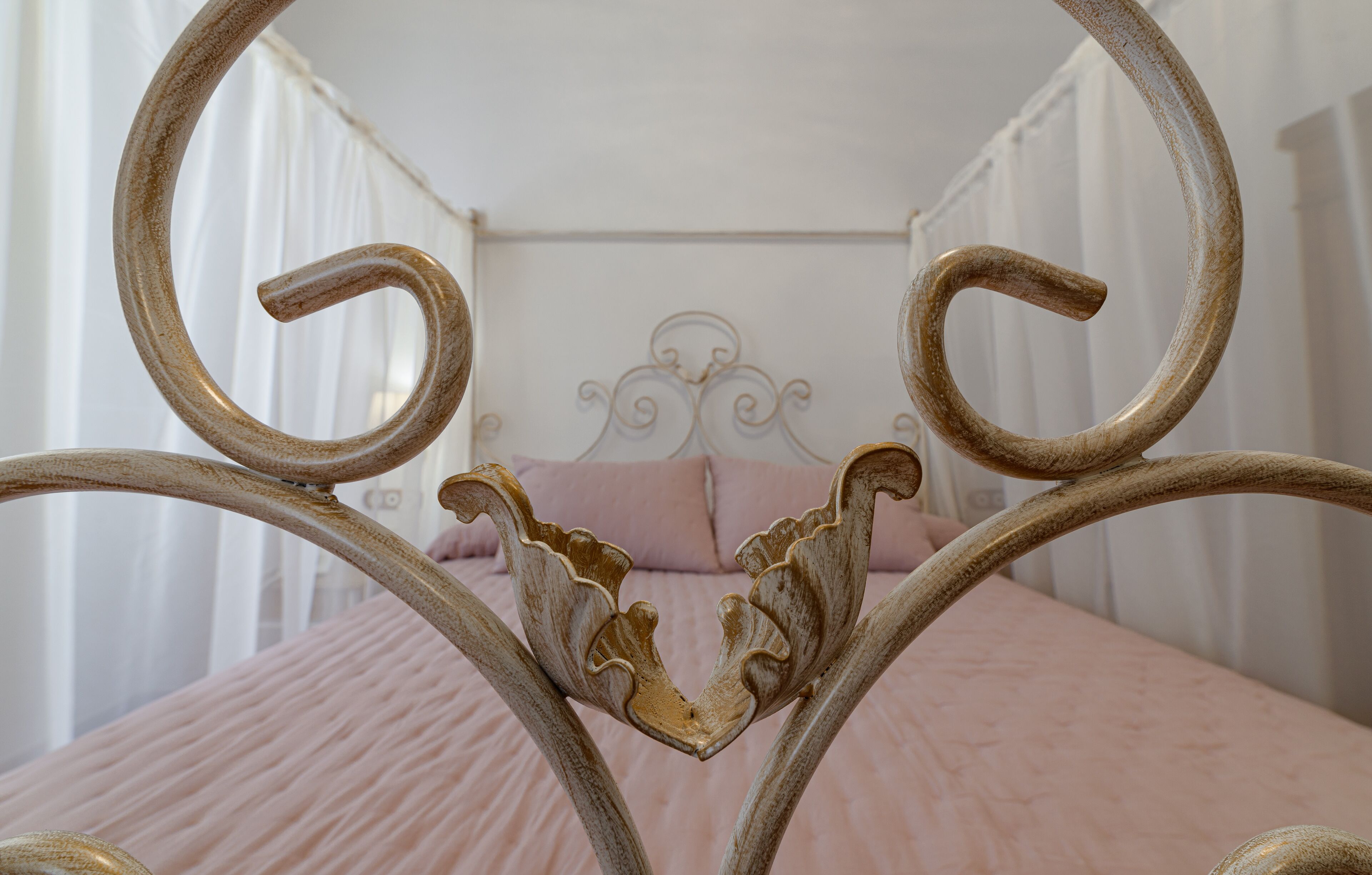 Una cama con cabecera, cortinas y una colcha rosa.