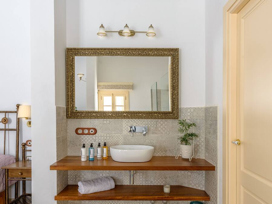 A bathroom with a large mirror, a white sink, and a wooden vanity. There are toiletries on the vanity and a towel hanging on the wall.