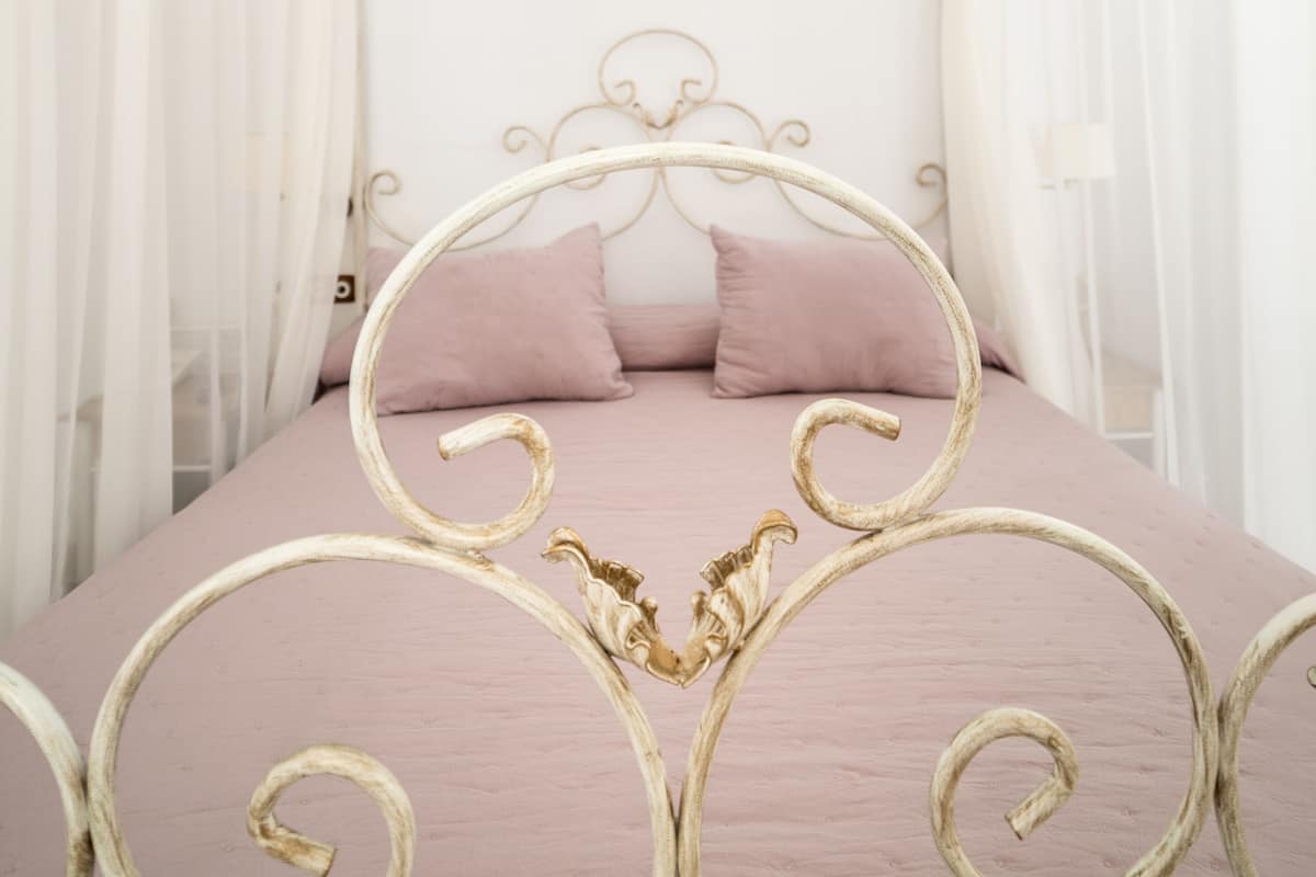 Ein Bett mit Metallgestell und einer rosa Decke, umgeben von weißen Vorhängen.