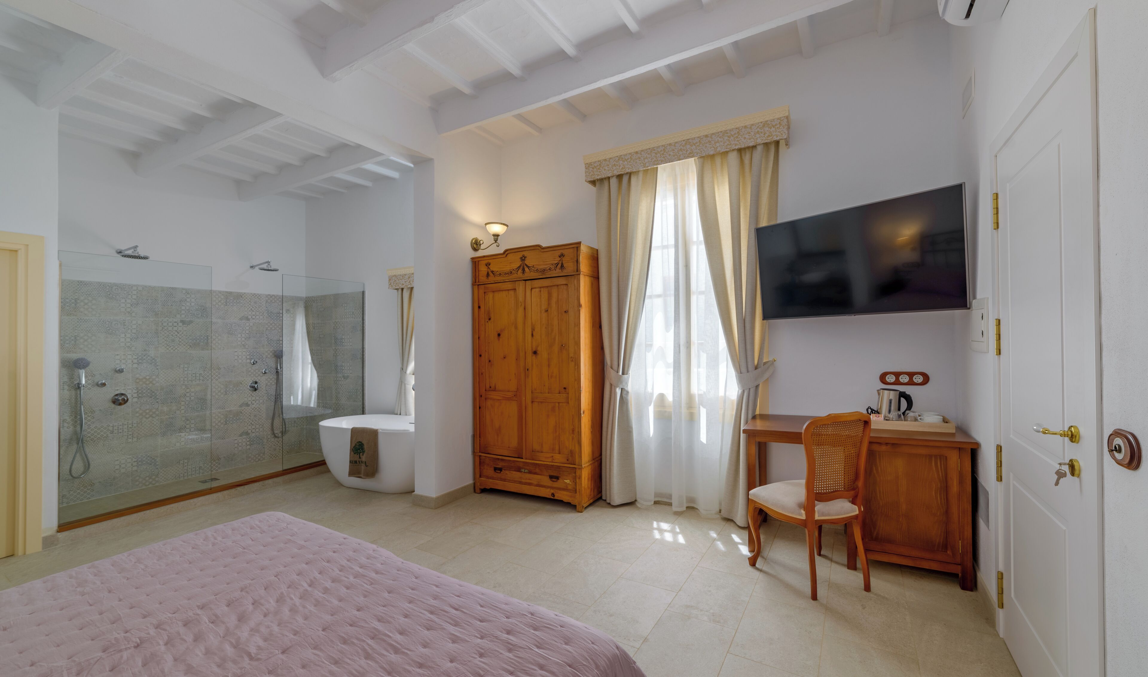 A bedroom with a bed, a desk, a TV, a wardrobe, and a shower area.