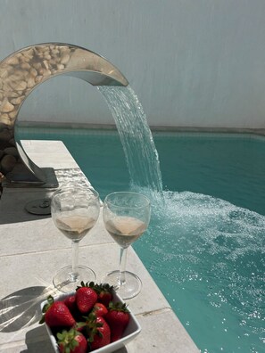 A poolside setting with a water feature, two glasses of white wine, and a bowl of strawberries. - Seranova Luxury Hotel - Adults Only (Ciutadella de Menorca)