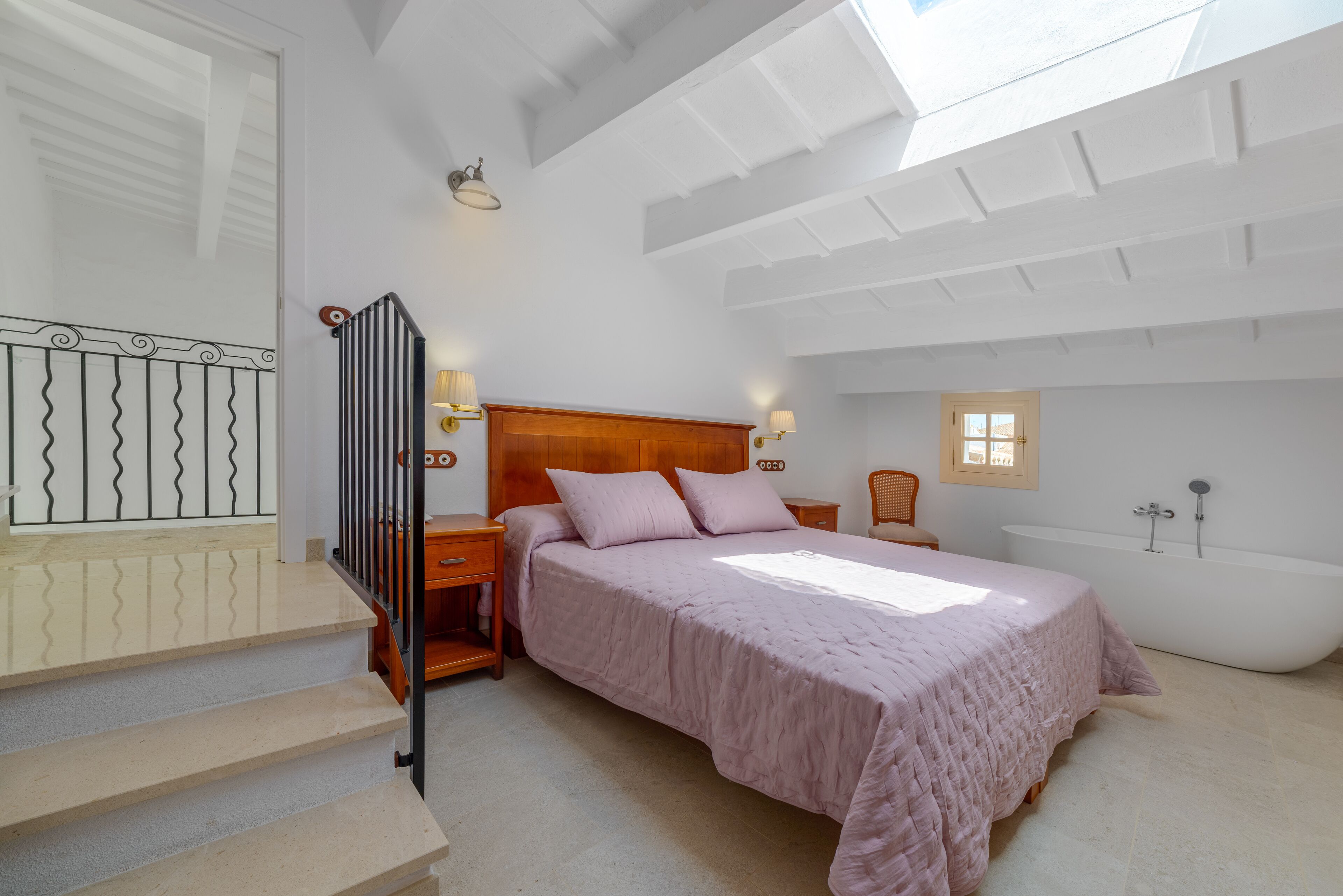 Un dormitorio con cama, mesita de noche, silla, ventana y bañera.