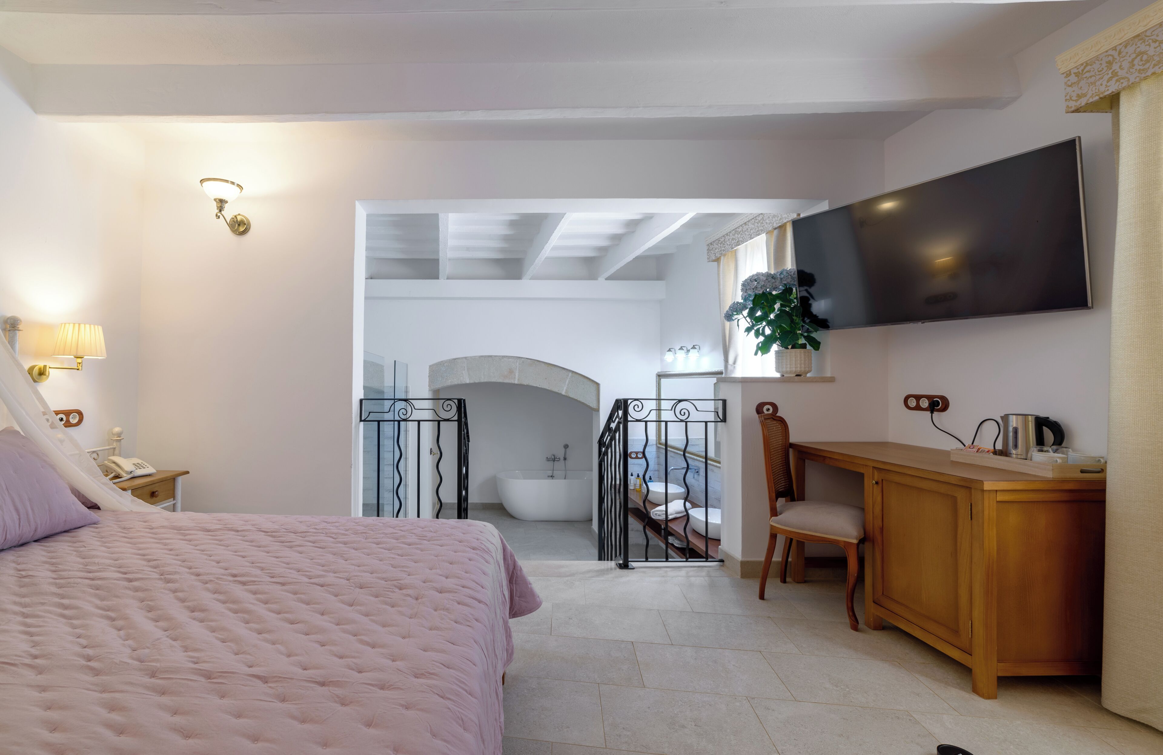 A bedroom with a bed, a desk, a TV, a bathroom with a bathtub, and a staircase.