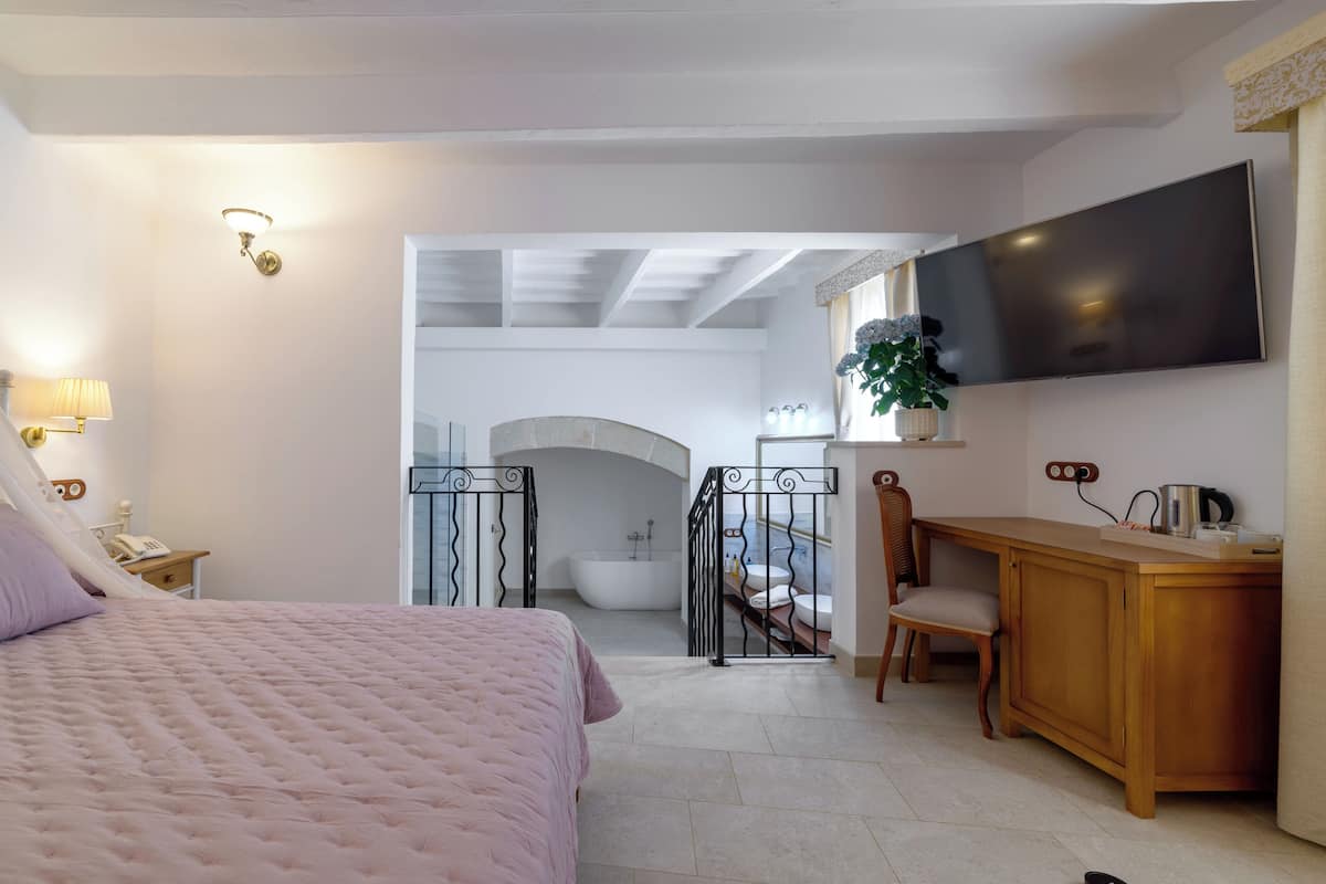 Ein Schlafzimmer mit Bett, Schreibtisch, Fernseher und einem Badezimmer mit Badewanne sowie einer Treppe.