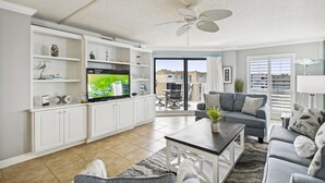 A modern living room with a flat-screen TV, white cabinetry, a ceiling fan, and a view to an outdoor balcony. - Inlet Reef 618 is Recently Upgraded 2 BR 2 Ba on the beach - amazing sunset views! by RedAwning (Destin)