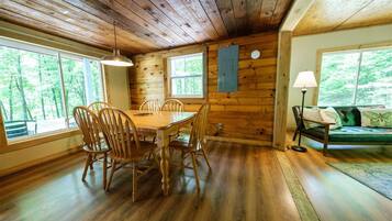 L’intérieur d’un chalet en bois comprend une table à manger, des chaises, un canapé et de grandes fenêtres.