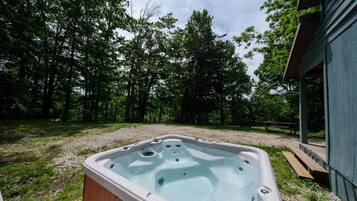 A hot tub in a wooded area with a wooden deck and a building in the background.