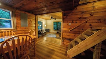 Un intérieur en bois comprenant un coin repas, un escalier et une vue sur le salon, accessible par une porte.