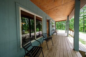 A covered porch with wooden flooring and metal chairs.
