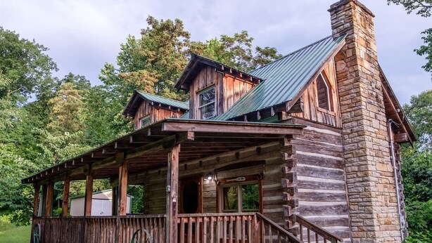 A log cabin with a porch, stone chimney, and a sign indicating a campground. - Log Cabin Getaway in the RRG. (Ravenna)