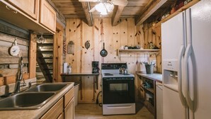 A kitchen with wooden walls, a stove, a sink, and a refrigerator. - Log Cabin Getaway in the RRG. (Ravenna)