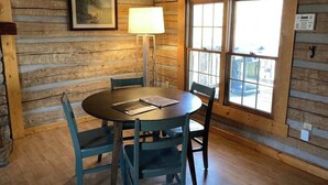 A wooden cabin interior with a round table, four chairs, a lamp, and a window with a view. - Log Cabin Getaway in the RRG. (Ravenna)