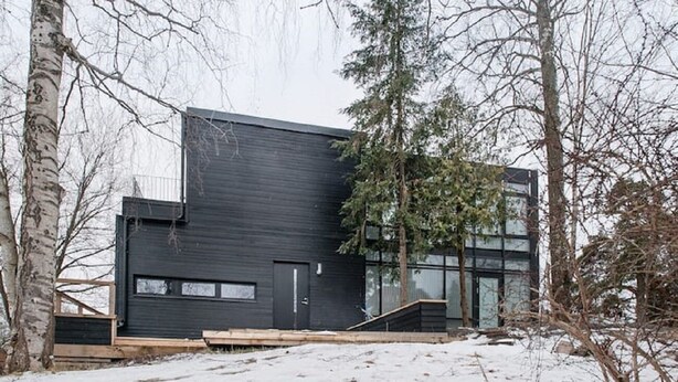 A modern building with a dark exterior, large windows, and a wooden deck.