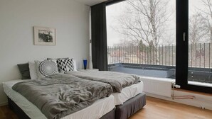 A bedroom with a large window, a bed, a radiator, and a picture on the wall.