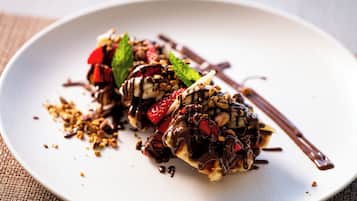 A dessert on a plate with chocolate drizzle and nuts.