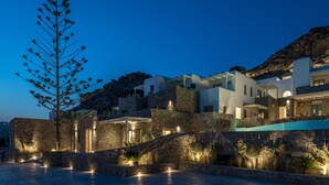 A coastal building with stone walls, a swimming pool, and a staircase leading to the upper levels. - Arocaria (Mykonos)