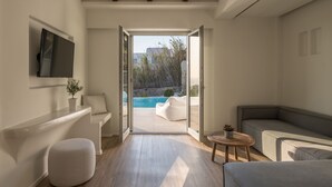 A modern living room with a large window, a sofa, a small table, and a TV mounted on the wall. - Arocaria (Mykonos)