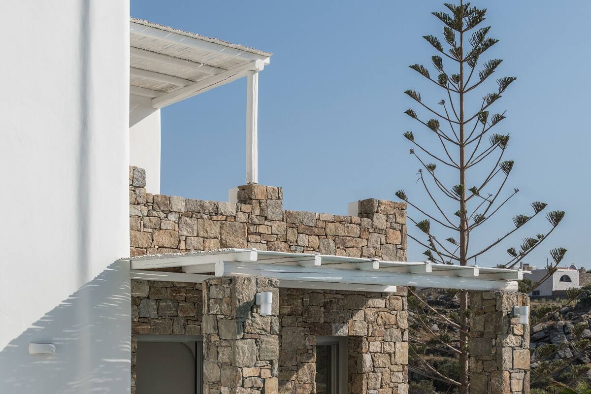 A modern outdoor pool area with stone walls, a white pergola, and a single bed with a view.