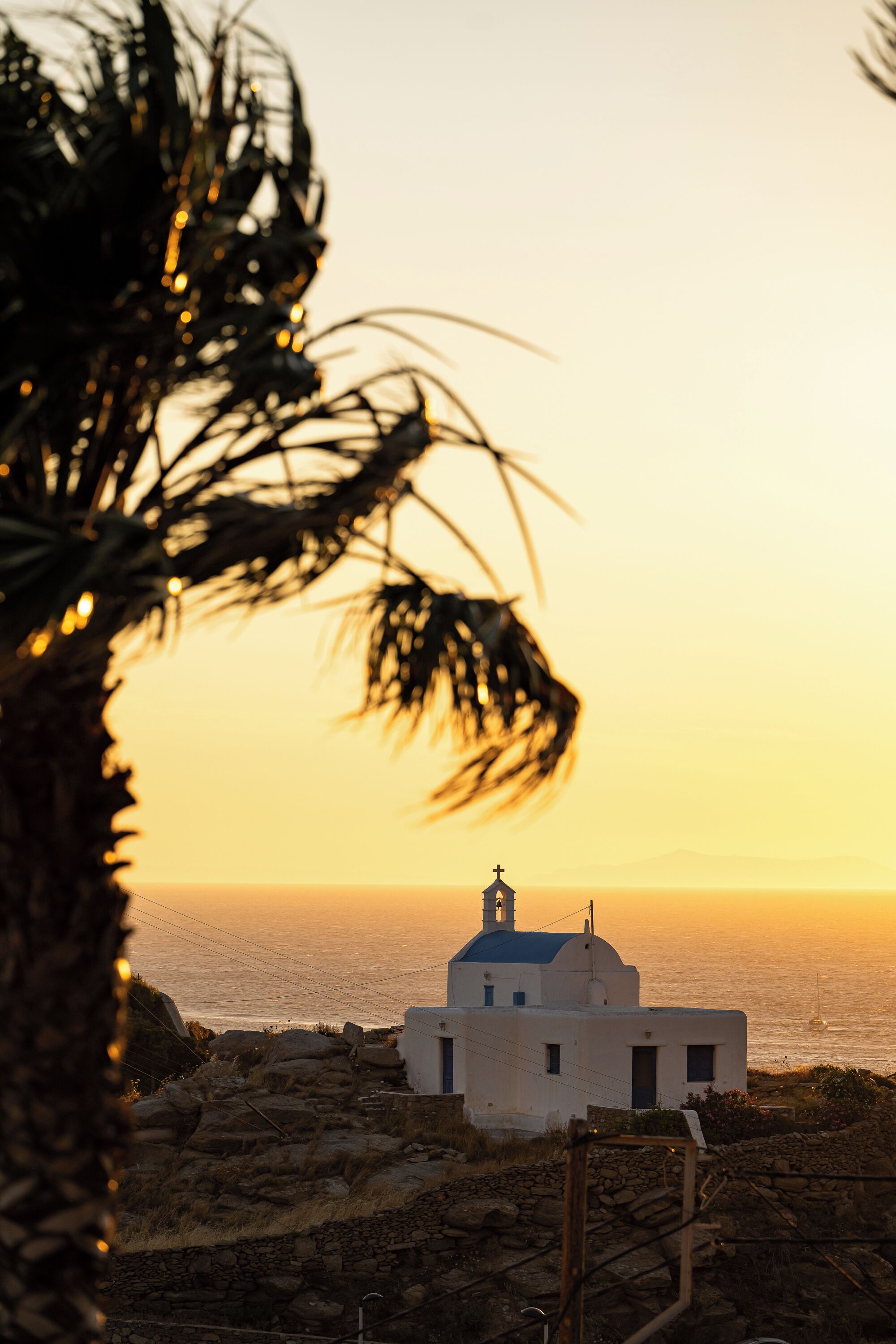 A coastal building with a dome and a bell tower, surrounded by rocky terrain and palm trees.