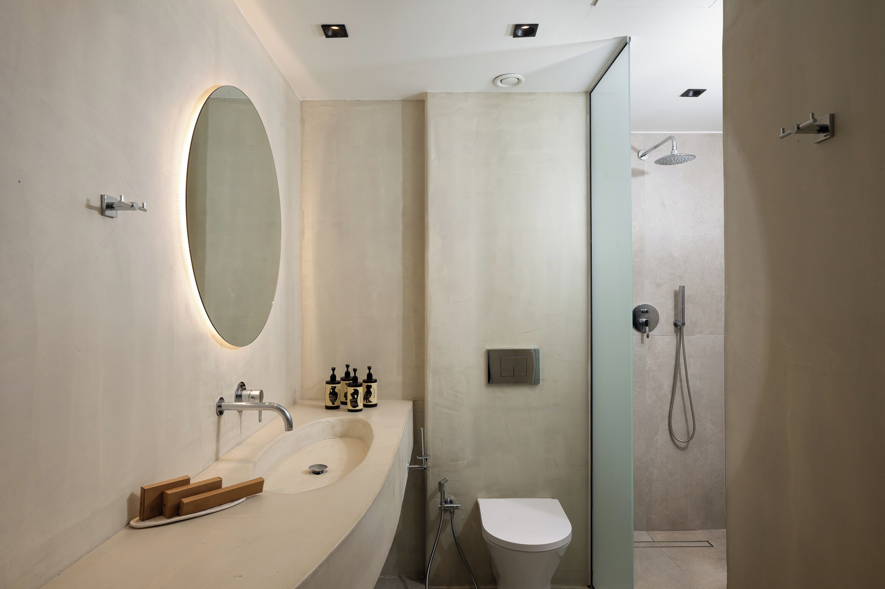 A modern bathroom with a large oval mirror, a sink, a toilet, and a shower area.
