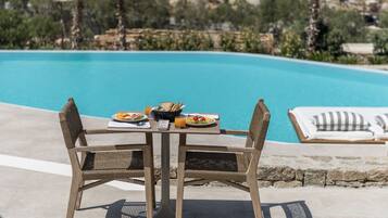 A dining table with wicker chairs and a view of a pool.