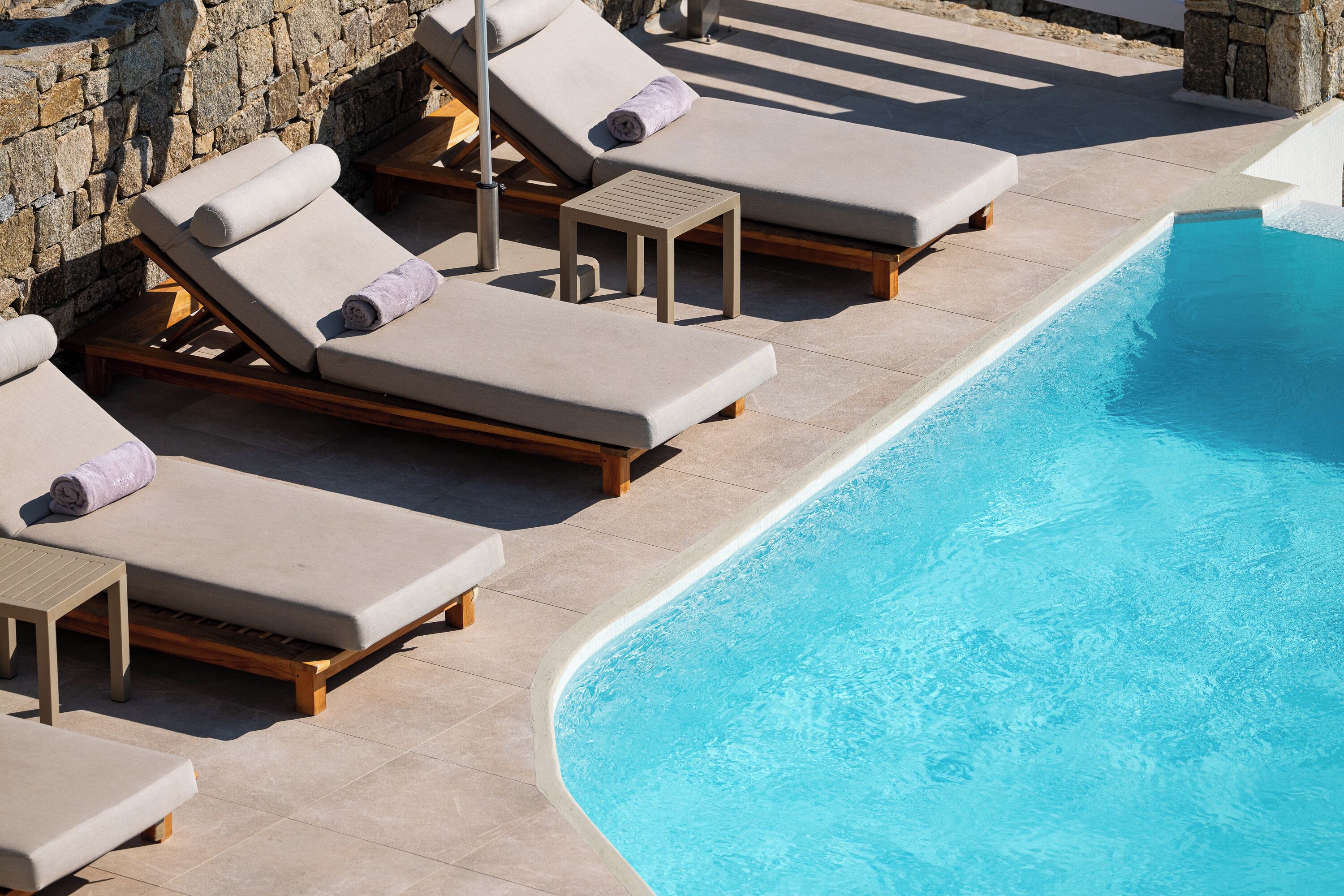 A poolside area with lounge chairs and a stone wall.