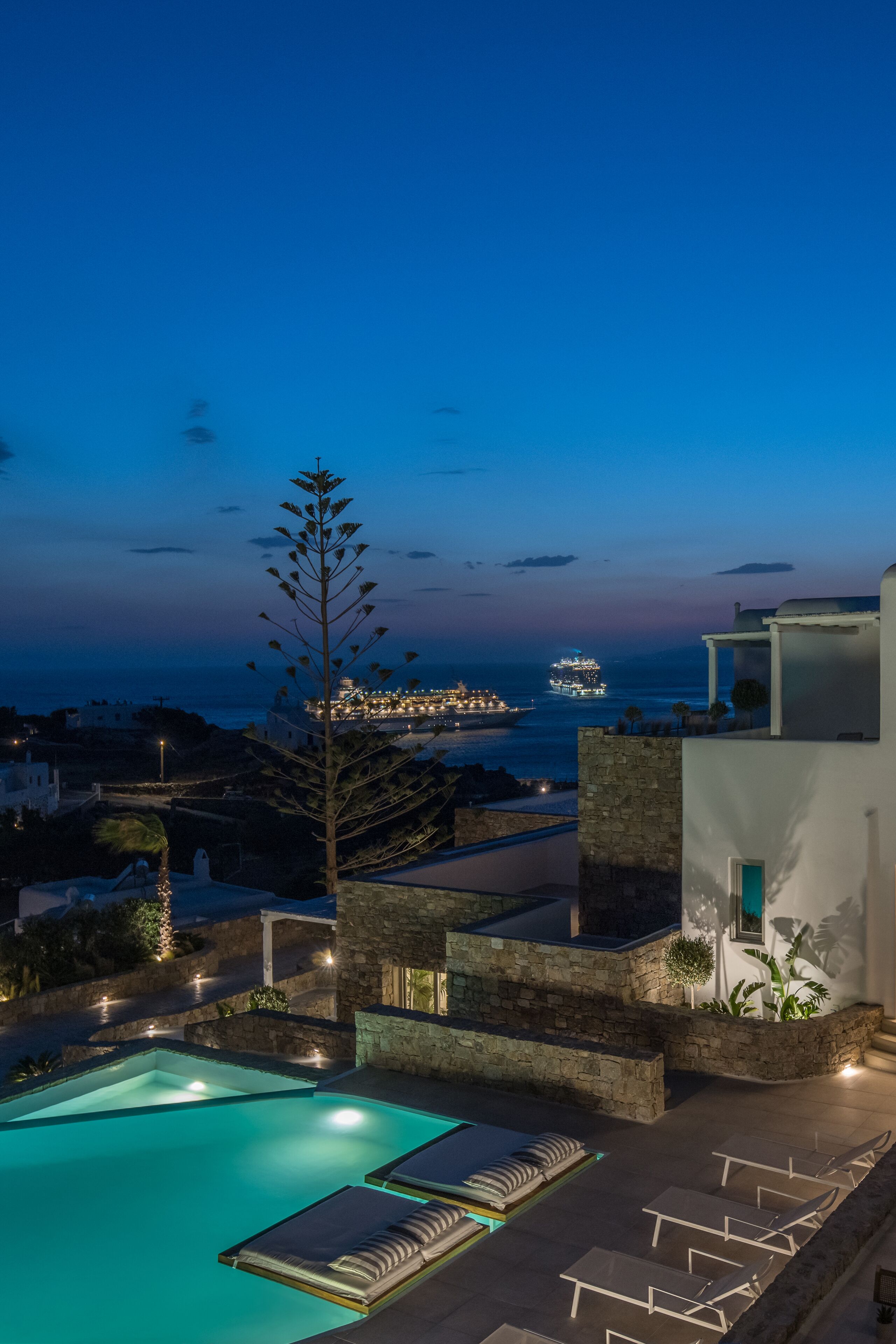 A pool area with lounge chairs and a view of the sea at dusk.