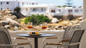 A table with two glasses of orange juice and a plate of food, wicker chairs, and white buildings in the background.