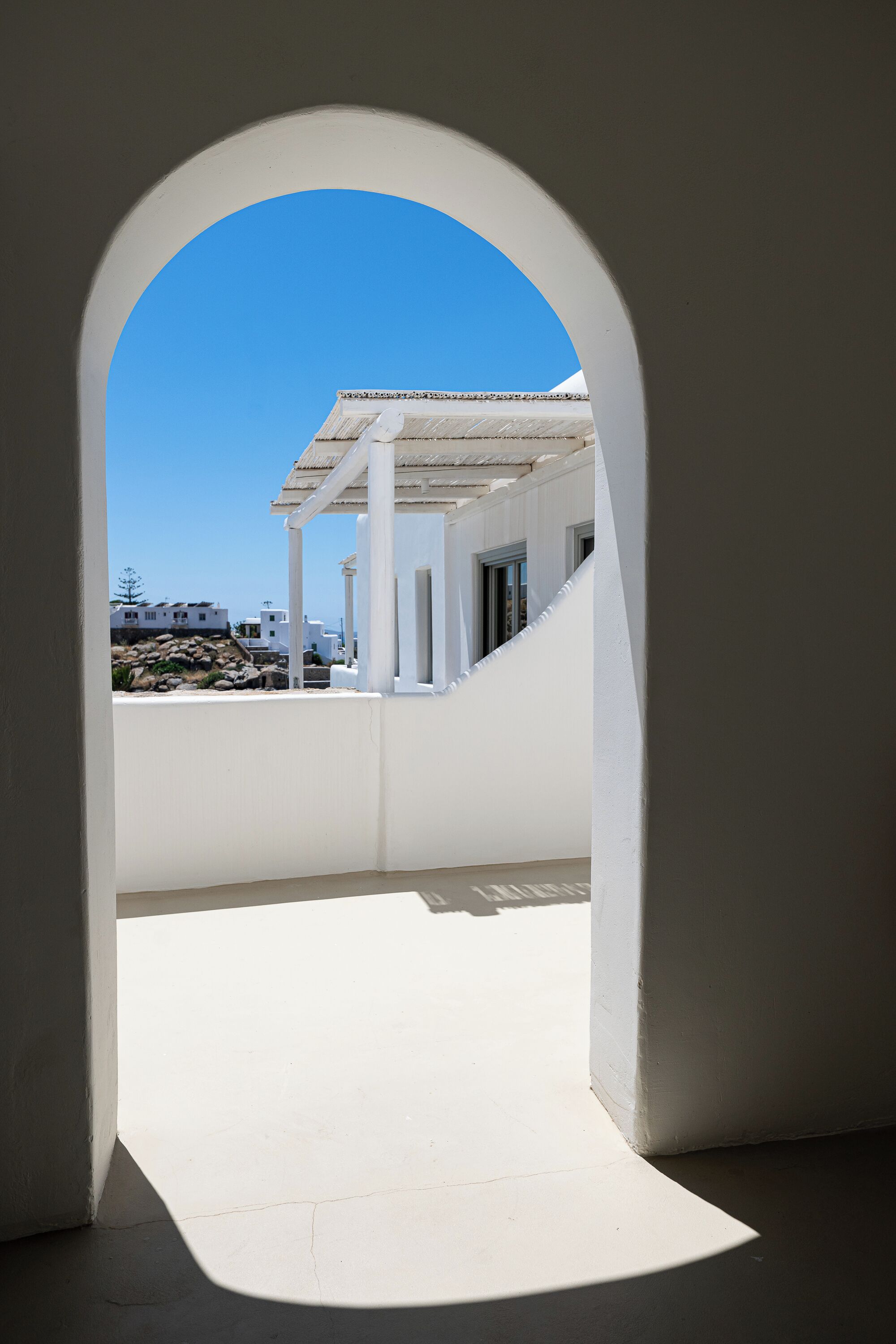 An arched doorway leading to a balcony with a clear view of a white building and a blue sky.