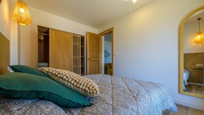 A bedroom with a patterned bedspread, a green pillow, and a beige accent pillow. There is a wooden wardrobe and a mirror on the wall. - Deluxe sea view apartment (Propriano)
