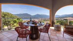 A balcony with a round table, wicker chairs, and a view of mountains and greenery. - Deluxe sea view apartment (Propriano)
