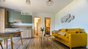 A modern living room with a yellow sofa, wooden dining table, and kitchen area with green cabinets. - Deluxe sea view apartment (Propriano)