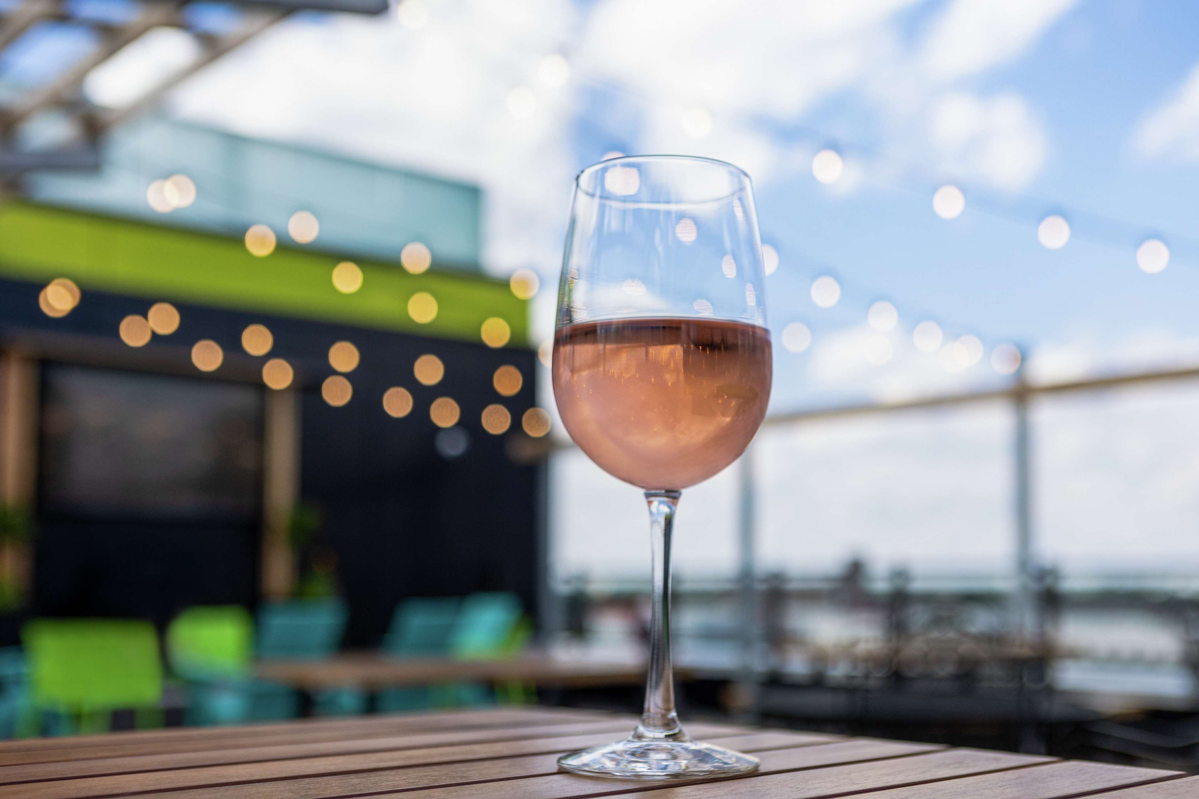 A glass of rosé wine on a wooden table with a blurred background of a restaurant or bar area.