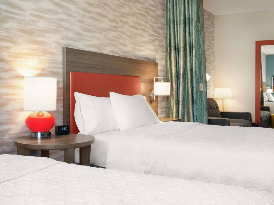 Une chambre d’hôtel avec un grand lit, deux tables de chevet, une lampe rouge et une horloge.