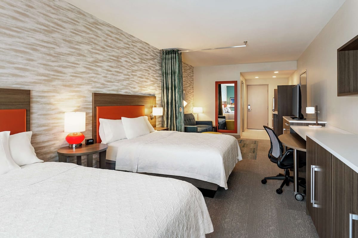Een hotelkamer met twee bedden, een bureau, een stoel, een televisie en een badkamer zichtbaar door een geopende deur.