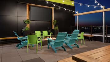 Un patio al aire libre con sillas Adirondack color turquesa, una mesa de madera y un brasero.