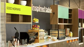 A breakfast bar with a "GOOD MORNING" sign, a waffle maker, and a display case with food items.
