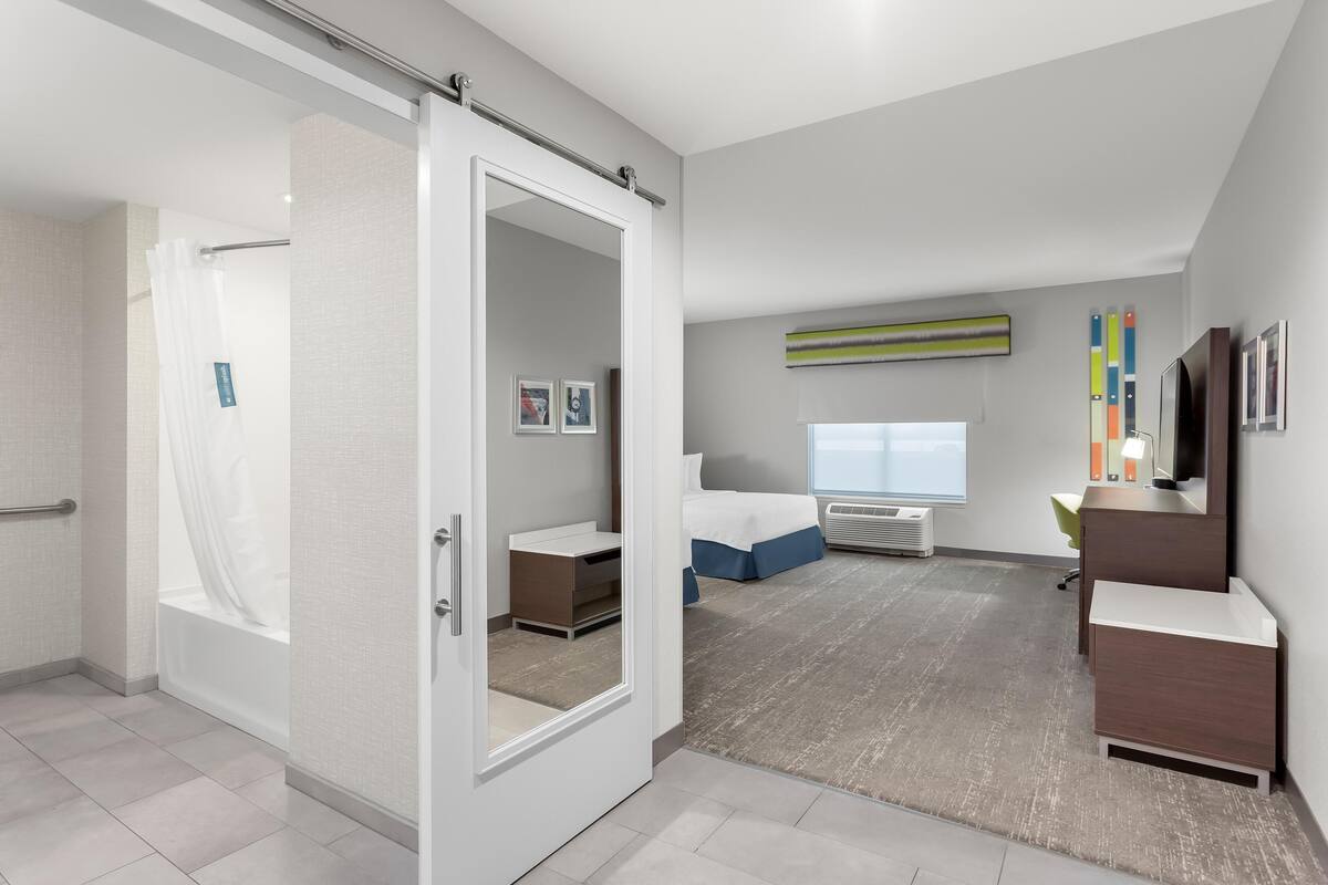 Quarto de hotel moderno com closet espaçoso, cama grande, escrivaninha e vista para a cidade.