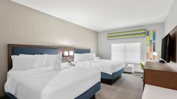 A hotel room with two beds, a TV, a desk, and a window with blinds.