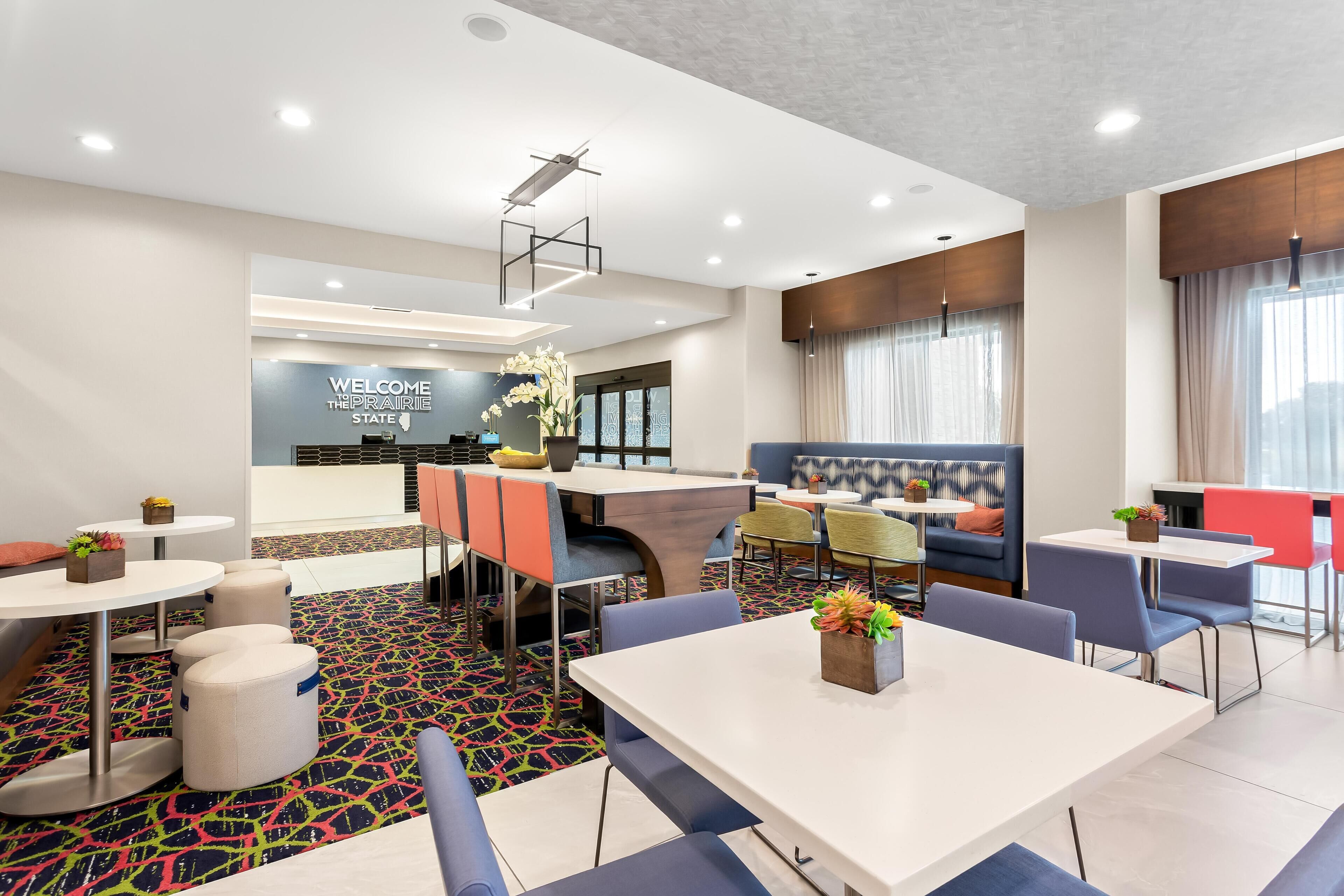 A modern hotel lobby with a reception desk, seating areas, and a colorful carpet.
