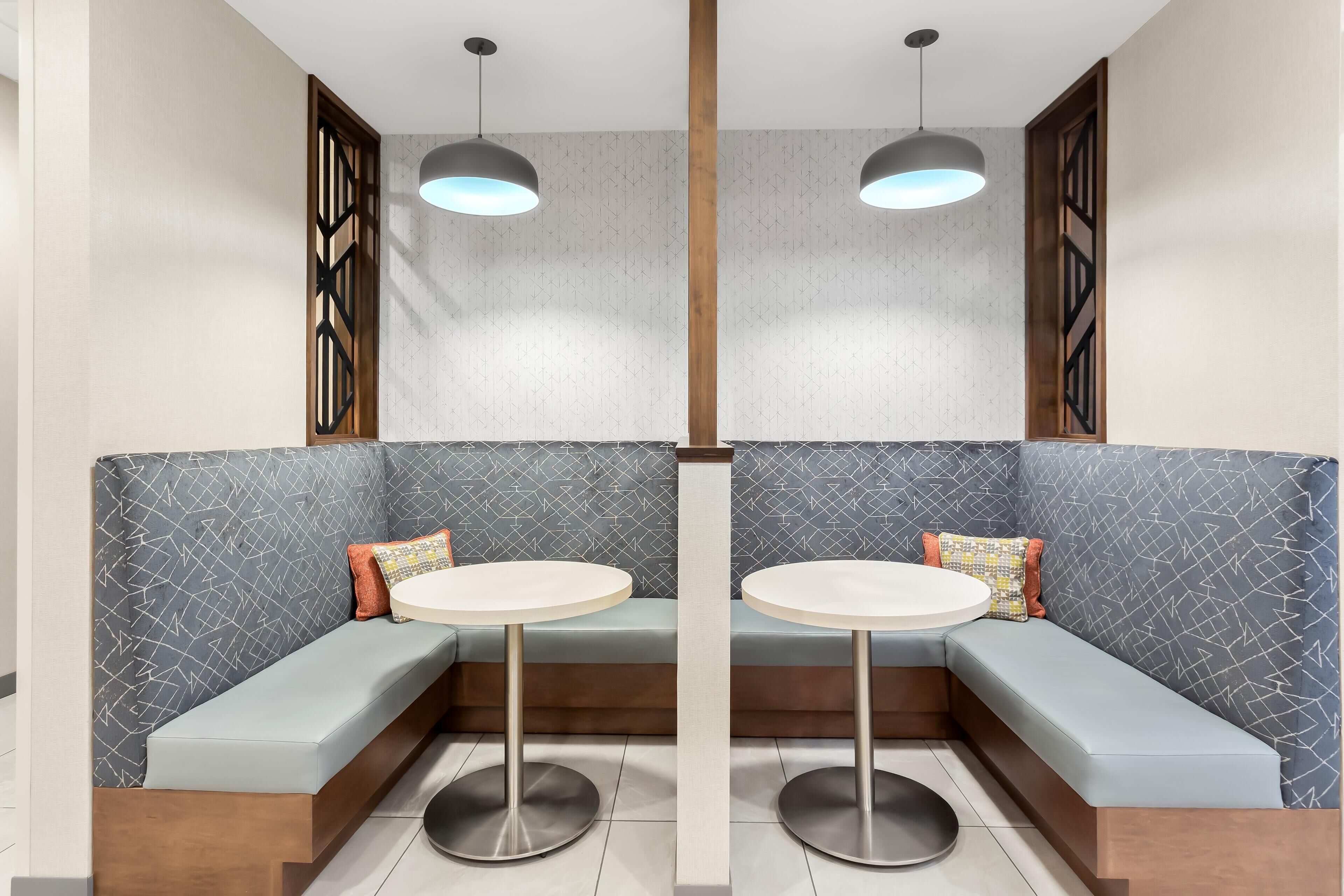A modern seating area with two round tables and benches, featuring geometric patterned walls and wooden accents.
