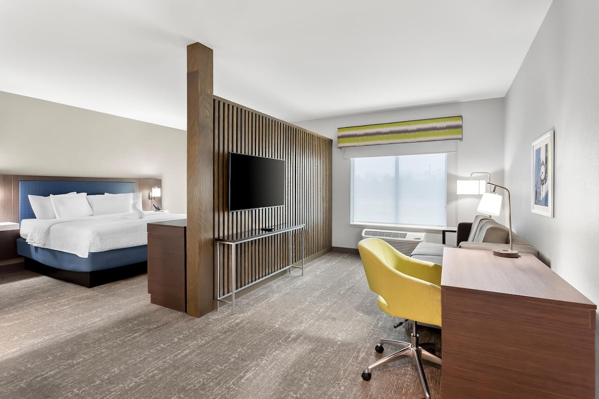 Quarto de hotel com cama, escrivaninha, cadeira, televisão e janela.