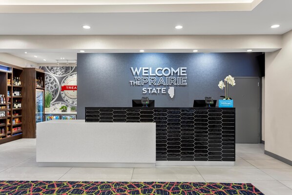 A reception desk with a "Welcome to the Prairie State" sign, a minibar, and a "Hilton" sign.