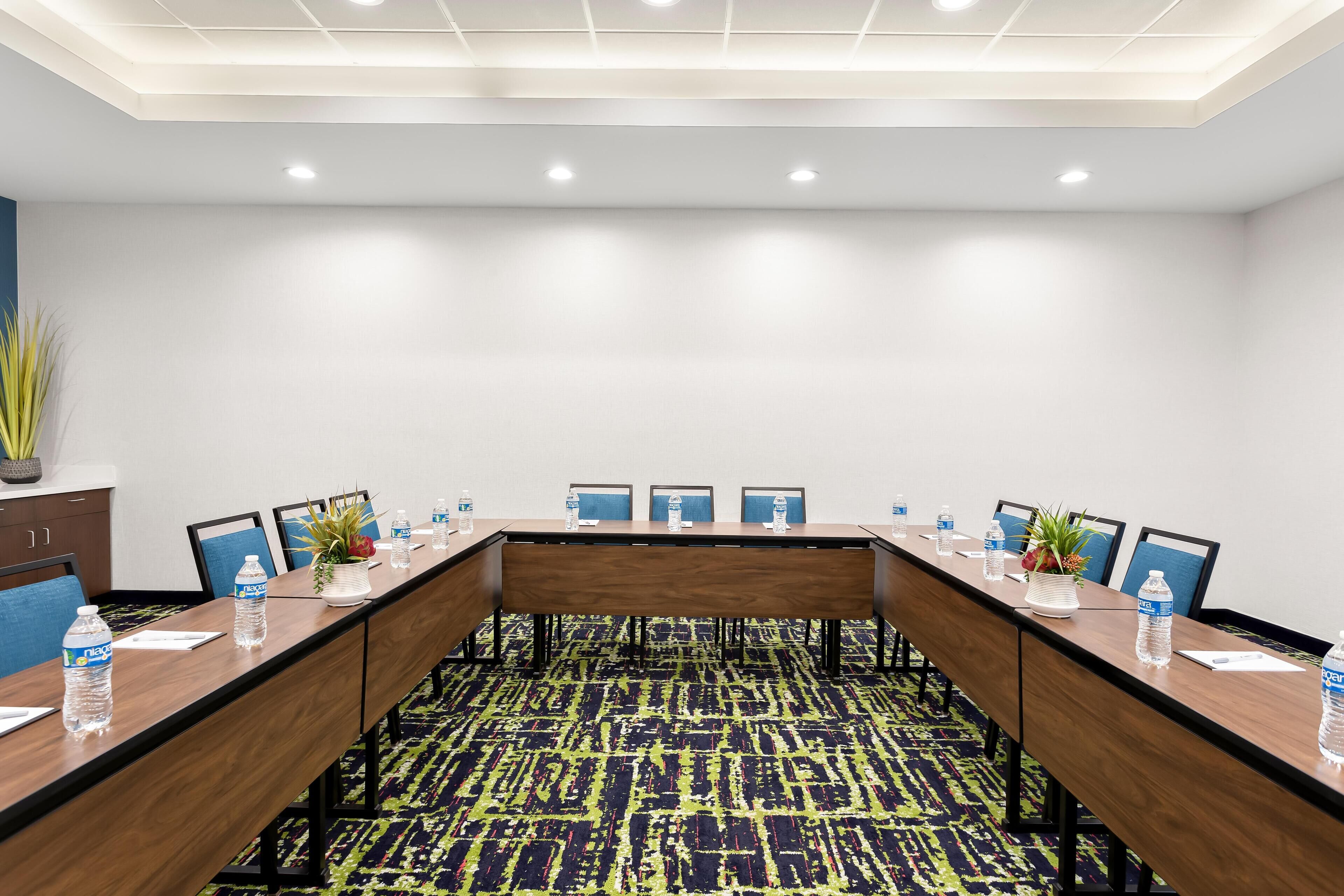 A conference room with a long table, chairs, water bottles, and a plant.