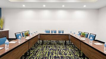 A conference room with a long table, chairs, water bottles, and a plant.